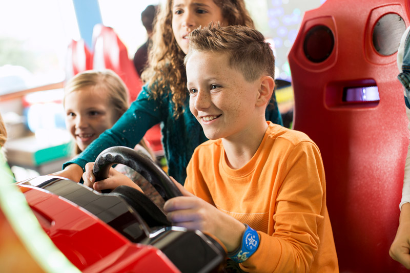 Child playing arcade racing game while two other children watch